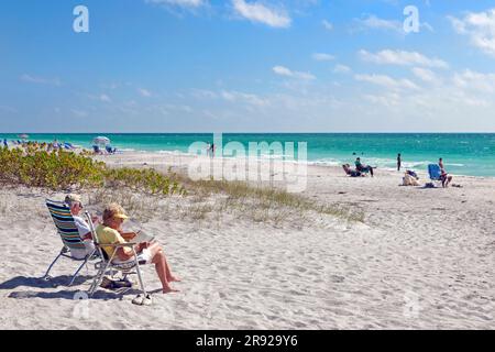 Couple senior retraité lisant sur la plage de Siesta Key, Sarasota, la côte ouest ou du golfe de Floride, États-Unis. Banque D'Images