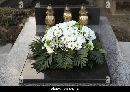 Couronne funéraire de fleurs et lanternes sur pierre tombale de granit dans le cimetière Banque D'Images