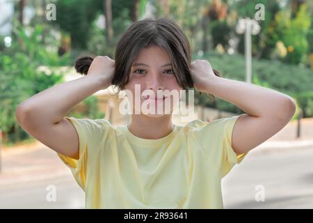 Une jeune fille dans un T-shirt jaune tient les cheveux dans les mains dans une queue de cheval. Banque D'Images