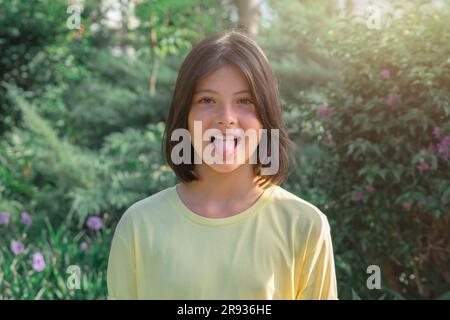 Portrait d'une jeune fille joyeuse et ludique qui montre sa langue. Sur fond de verdure dans le parc de la ville. Banque D'Images