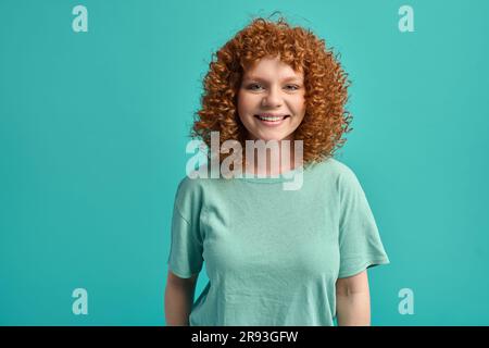 Bonne bonne positive souriante redée adolescente avec des cheveux bouclés regardant l'appareil photo Banque D'Images