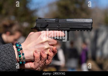 Main femelle avec bracelet tenant un pistolet automatique noir Banque D'Images