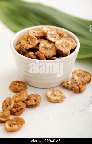 Tranches de banane fraîches et biologiques séchées dans un bol en verre avec une feuille verte. Banque D'Images