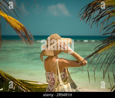 Jeune femme gaie portant un chapeau tendance sur une plage pittoresque aux Maldives Banque D'Images