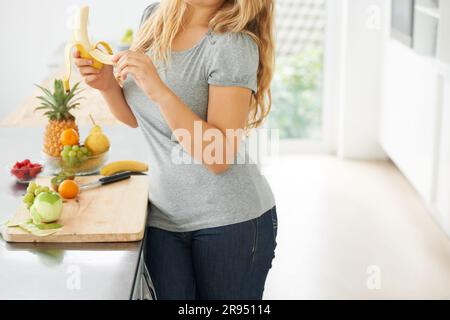 Fruits, banane à éplucher ou femme avec un en-cas sain le matin, repas de petit déjeuner ou repas du midi dans la cuisine maison. Mains, corps ou fille végétalienne manger de la nourriture à perdre Banque D'Images