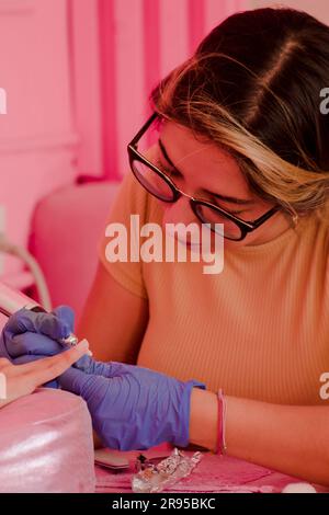 Une manucure féminine gaie portant des lunettes applique un vernis à ongles rose vif à un client dans le salon Banque D'Images