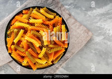 Pâtes fusilli colorées au blé dur sur fond gris. Macaroni en spirale multicolore dans un bol Banque D'Images