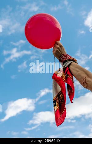 Une main levée au ciel avec un ballon rouge et une écharpe enroulée autour du poignet Banque D'Images