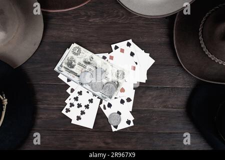 Vieux chapeaux de l'Ouest avec carte à jouer avec des papiers argent et pièces d'argent sur la table. Vue de dessus. Banque D'Images