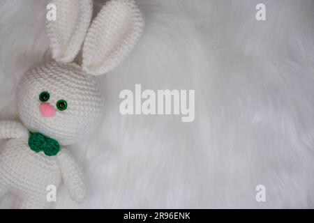 Animaux en crochet farcis. Joli lapin blanc tricoté avec noeud papillon vert et nez rose se trouve sur un fond de laine molletonnée. Vue de dessus, bannière Web avec Banque D'Images