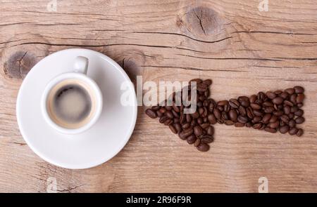 Flèche faite de grains de café pointant vers une tasse de café remplie, le tout sur une vieille planche en bois, arrangement horizontal Banque D'Images