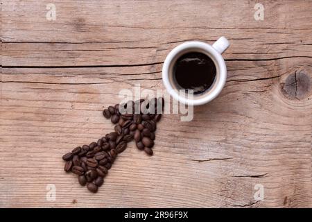 Flèche faite de grains de café pointant vers une tasse de café remplie, le tout sur une vieille planche en bois, disposition diagonale Banque D'Images