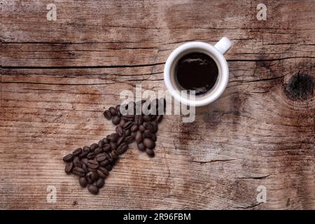 Flèche faite de grains de café pointant vers une tasse de café remplie, le tout sur une vieille planche en bois, disposition diagonale Banque D'Images