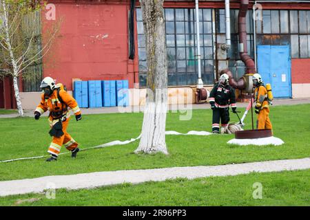 Les pompiers professionnels, les sauveteurs en combinaisons de protection ignifuges, les casques et les masques à gaz sont prêts à sauver des personnes du danger avec un tuyau d'incendie, a Banque D'Images