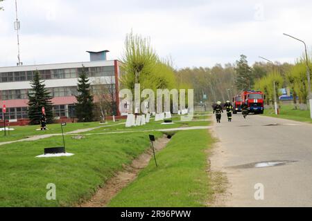 Un grand véhicule de secours incendie rouge, un camion pour éteindre un incendie et des pompiers mâles dans une raffinerie de produits chimiques et de pétrole sur fond d'arbres. Banque D'Images