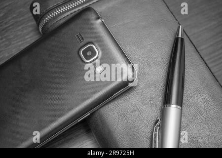 Accessoires pour hommes avec un portefeuille, un stylo, un smartphone sur l'arrière-plan de la table photo en noir et blanc Banque D'Images