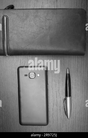 Accessoires pour hommes avec un portefeuille, un stylo, un smartphone sur l'arrière-plan de la table photo en noir et blanc Banque D'Images