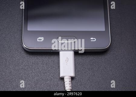 smartphone noir sur fond noir mat avec un câble blanc connecté Banque D'Images