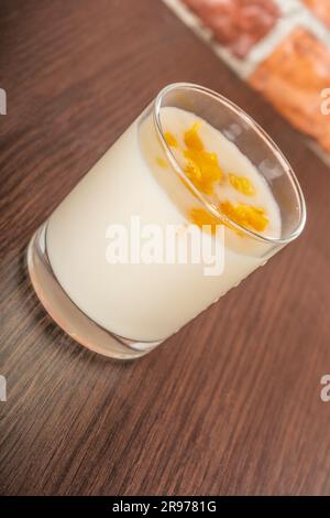 yaourt avec confiture d'orange et tranches dans une tasse de verre sur une table rustique en bois sur un fond de mur de brique Banque D'Images