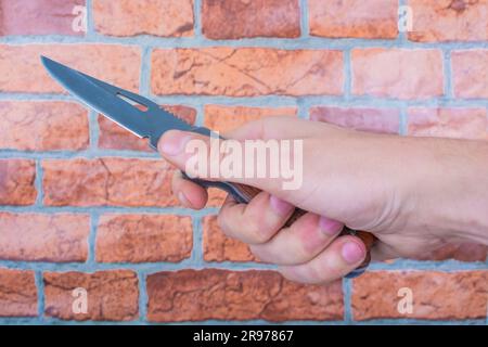 couteau pliant dans les mains des hommes, contre un fond de mur orange de brique Banque D'Images