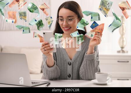 Paiement en ligne. Femme avec carte de crédit achetant quelque chose en utilisant le téléphone mobile à la maison. Les billets en euros sortent du gadget comme processus de transaction de l'argent Banque D'Images