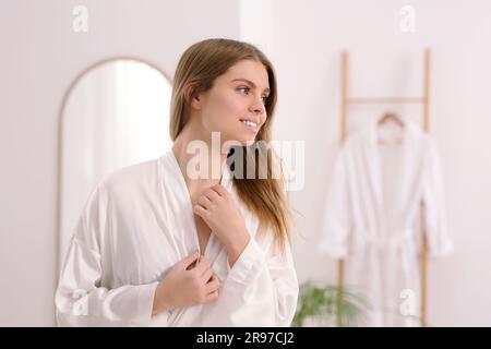 Belle femme heureuse portant un élégant peignoir blanc dans la salle de bains Banque D'Images