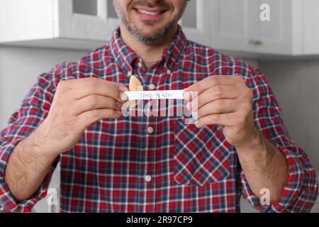 L'homme heureux tenant un cookie de fortune savoureux avec le temps de prévision est maintenant à l'intérieur, gros plan Banque D'Images