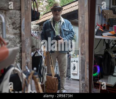 Kotor, Monténégro, 13 avril 2023 : photographe avec un chapeau debout à côté des étals du bazar de rue dans la vieille ville Banque D'Images