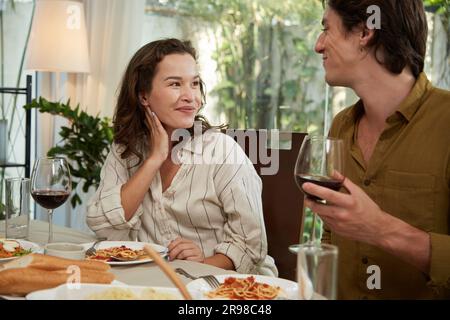 Bonne jeune femme regardant le petit ami quand ils mangent le dîner à la maison Banque D'Images