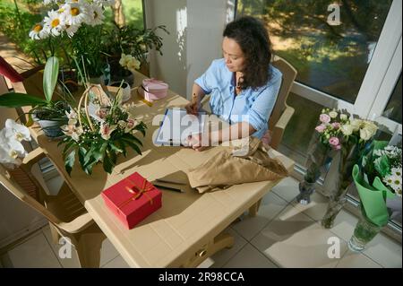 Vue de dessus de la vendeuse féminine en fleuriste, fleuriste avec presse-papiers, réception de la commande. Concept de personnes et de petites entreprises Banque D'Images