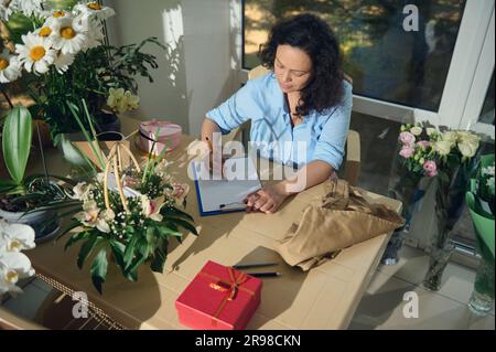 Vue depuis le dessus d'une fleuriste féminine avec presse-papiers, recevoir la commande pour des événements spéciaux de la vie de fête, écrire des notes Banque D'Images