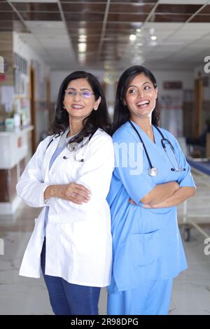 Plan de profil complet d'une femme médecin indienne debout dos à dos. Médecin senior en costume blanc et infirmière en uniforme bleu. Banque D'Images