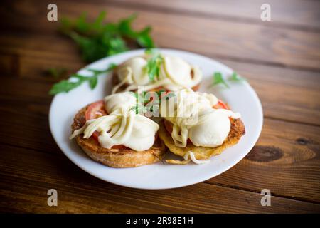 frits dans des croque-monsieur avec tomates et mozzarella dans une assiette avec herbes, sur une table en bois. Banque D'Images