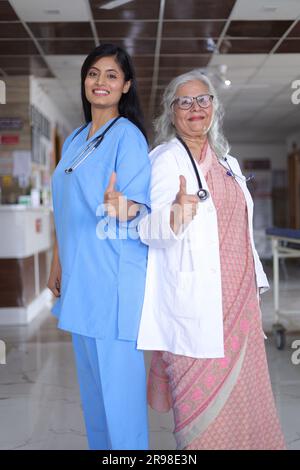 Plan de profil complet d'une femme médecin indienne debout dos à dos. Médecin senior en costume blanc et infirmière en uniforme bleu. Banque D'Images