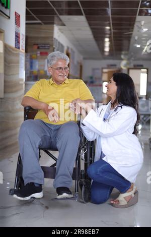 Infirmière indienne regardant très heureuse saluant un patient âgé dans un fauteuil roulant à l'hôpital et souriant - concepts de soins de santé. Banque D'Images