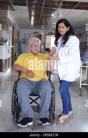 Infirmière indienne regardant très heureuse saluant un patient âgé dans un fauteuil roulant à l'hôpital et souriant - concepts de soins de santé. Banque D'Images