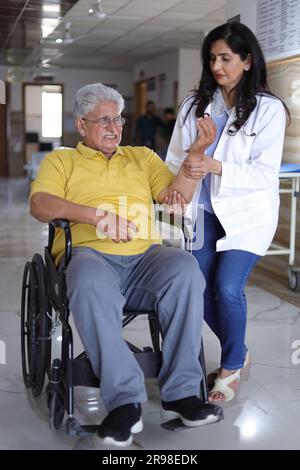 Infirmière indienne regardant très heureuse saluant un patient âgé dans un fauteuil roulant à l'hôpital et souriant - concepts de soins de santé. Banque D'Images