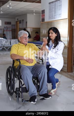 Infirmière indienne regardant très heureuse saluant un patient âgé dans un fauteuil roulant à l'hôpital et souriant - concepts de soins de santé. Banque D'Images