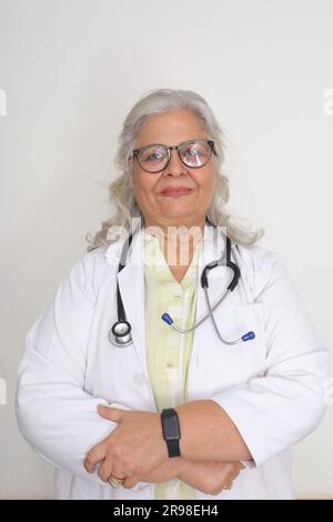 Médecin femme senior en blouse de laboratoire avec les bras croisés sur fond blanc. Heureux docteur indien en manteau blanc. confiant. Banque D'Images