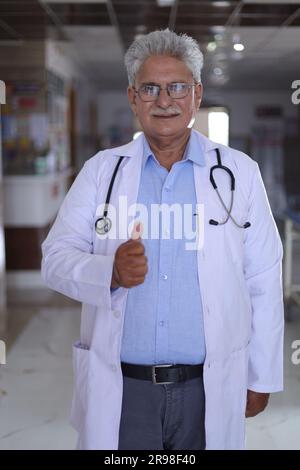 Portrait d'un médecin souriant en blouse de laboratoire montrant les pouces vers le haut. Heureux médecin senior en manteau blanc souriant sur fond de couloir d'hôpital. confiant. Banque D'Images