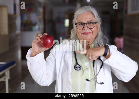 dépeignant le message d'avoir une meilleure santé et un régime très sain. Médecin féminin attrayant avec un manteau blanc souriant et tenant une pomme. Banque D'Images