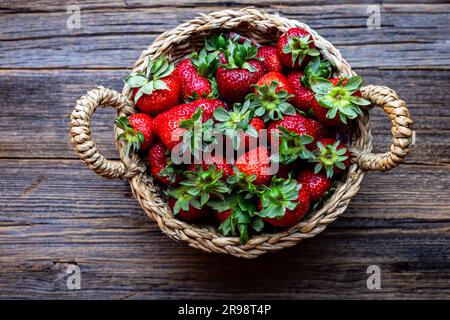 Fraises rouges fraîches, fraises biologiques dans un panier en osier sur fond de bois, vue sur le dessus. Banque D'Images