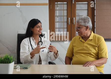 Attrayant jeune médecin indien assis avec un patient âgé dans le salon d'une maison de soins infirmiers. Un patient âgé ayant une conversation détaillée Banque D'Images