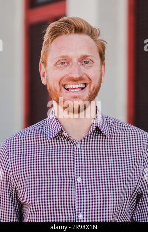 Portrait vertical individuel d'un classique joyeux redhead formel gars debout à l'extérieur souriant et regardant l'appareil photo. Vue de face d'un jeune adulte positif, un homme riant avec une expression amicale. Photo de haute qualité Banque D'Images