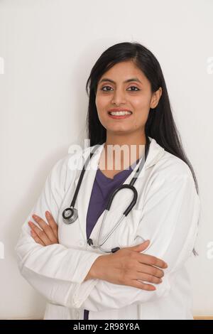Portrait d'indienne souriante médecin senior en blouse de laboratoire avec les bras croisés sur fond bleu. Heureux docteur indien en manteau blanc souriant sur ho Banque D'Images