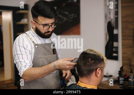 coiffeur barbu coupant les cheveux d'un client masculin. Coiffeur au service du client au salon de coiffure. Banque D'Images