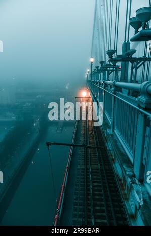 Un train passe sous un pont couvert de brouillard, créant une atmosphère mystérieuse et sinistre Banque D'Images