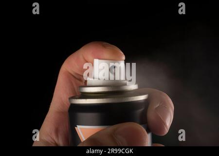 Vue rapprochée d'une main humaine et d'un flacon de spray pressé isolé sur fond noir Banque D'Images