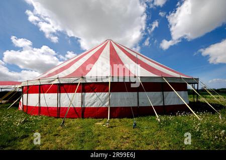 Une tente rouge et blanche de cirque à rayures dans une nature verte. Le ciel est bleu avec des cumulus blancs Banque D'Images
