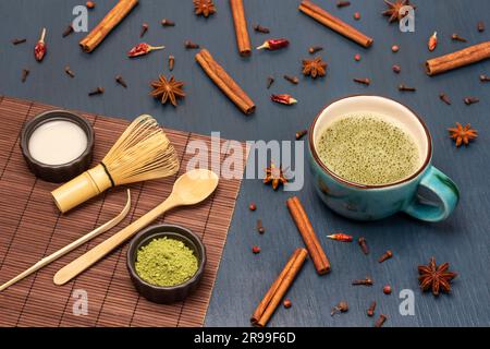 Thé vert de Matcha et épices sur la table. Cuillère de mesure, fouet, poudre de matcha verte dans un bol. Arrière-plan bleu Banque D'Images